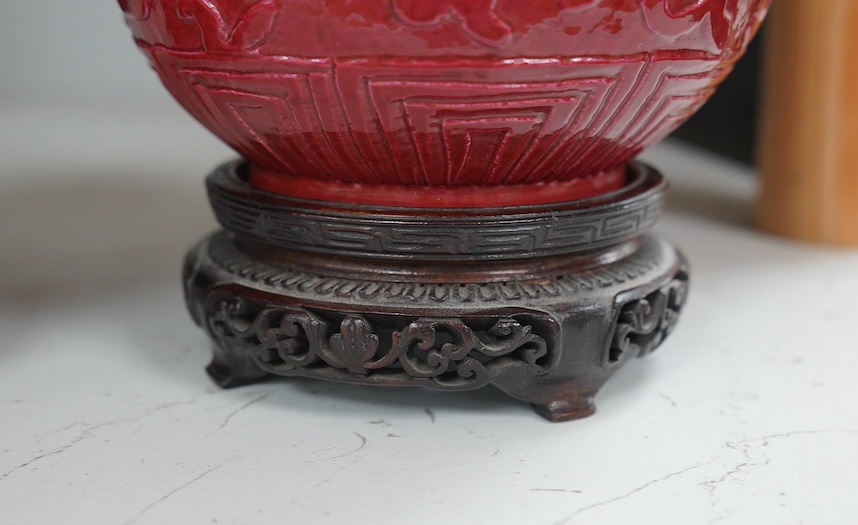 A pair of Chinese ruby ground ‘lotus’ bottle vases, late 19th century, each carved in relief with lotus flowers, scrolling tendrils and leaves, both with carved stands, 24cm high. Condition - one vase the neck broken bot